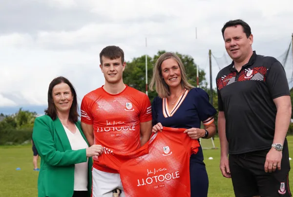 2 employees from JJ O'Toole, the coach and a player grouped together holding the new training kit - red, branded with JJ O'Toole.