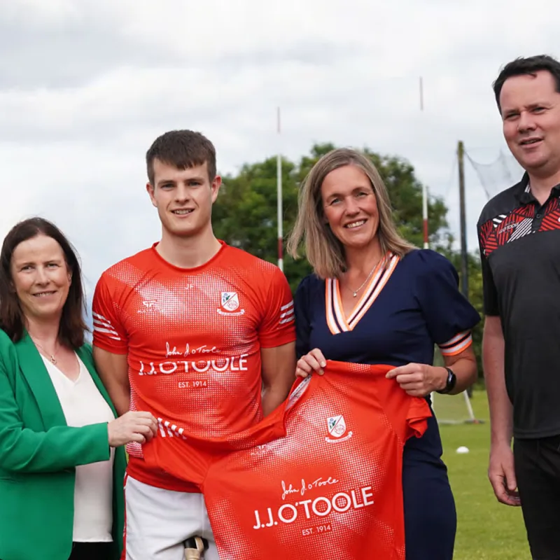 2 employees from JJ O'Toole, the coach and a player grouped together holding the new training kit - red, branded with JJ O'Toole.