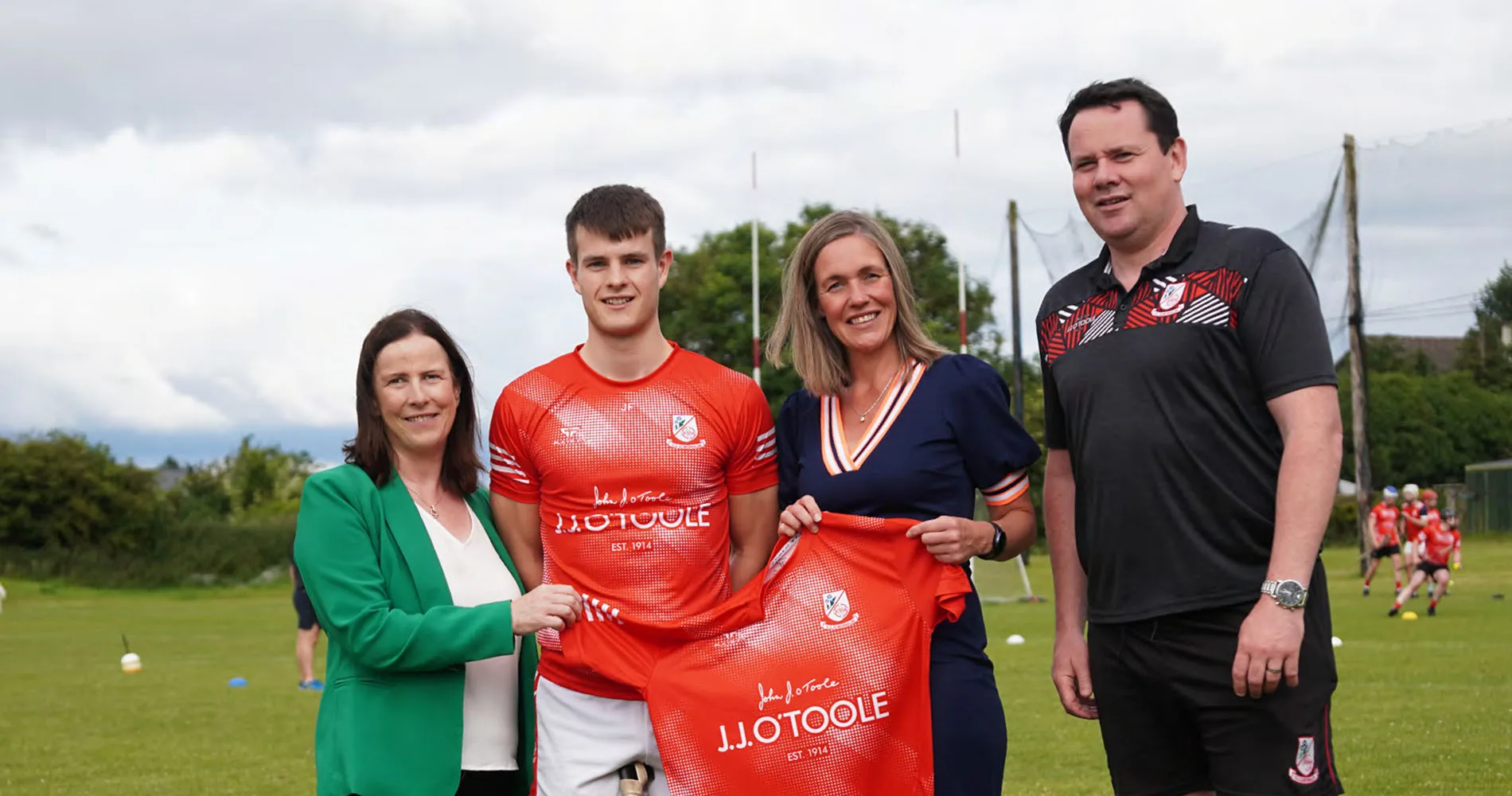 2 employees from JJ O'Toole, the coach and a player grouped together holding the new training kit - red, branded with JJ O'Toole.